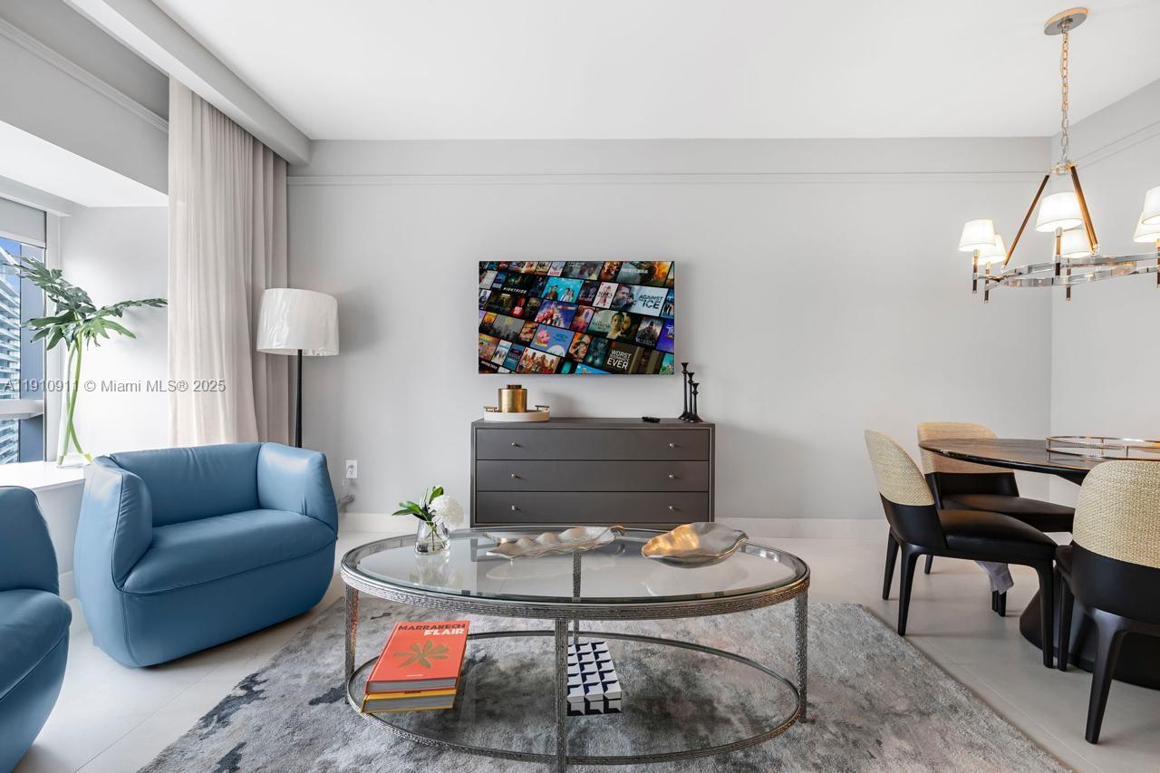 A living and dining area features a blue armchair, glass coffee table, and wall-mounted television — 1435 Brickell Ave # 3410, Miami FL 33131, MIAMI, FL