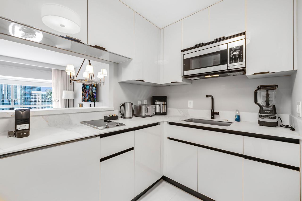 A modern kitchen features white cabinetry, black hardware, a stainless steel microwave, and marble countertops — 1435 Brickell Ave # 3410, Miami FL 33131, MIAMI, FL