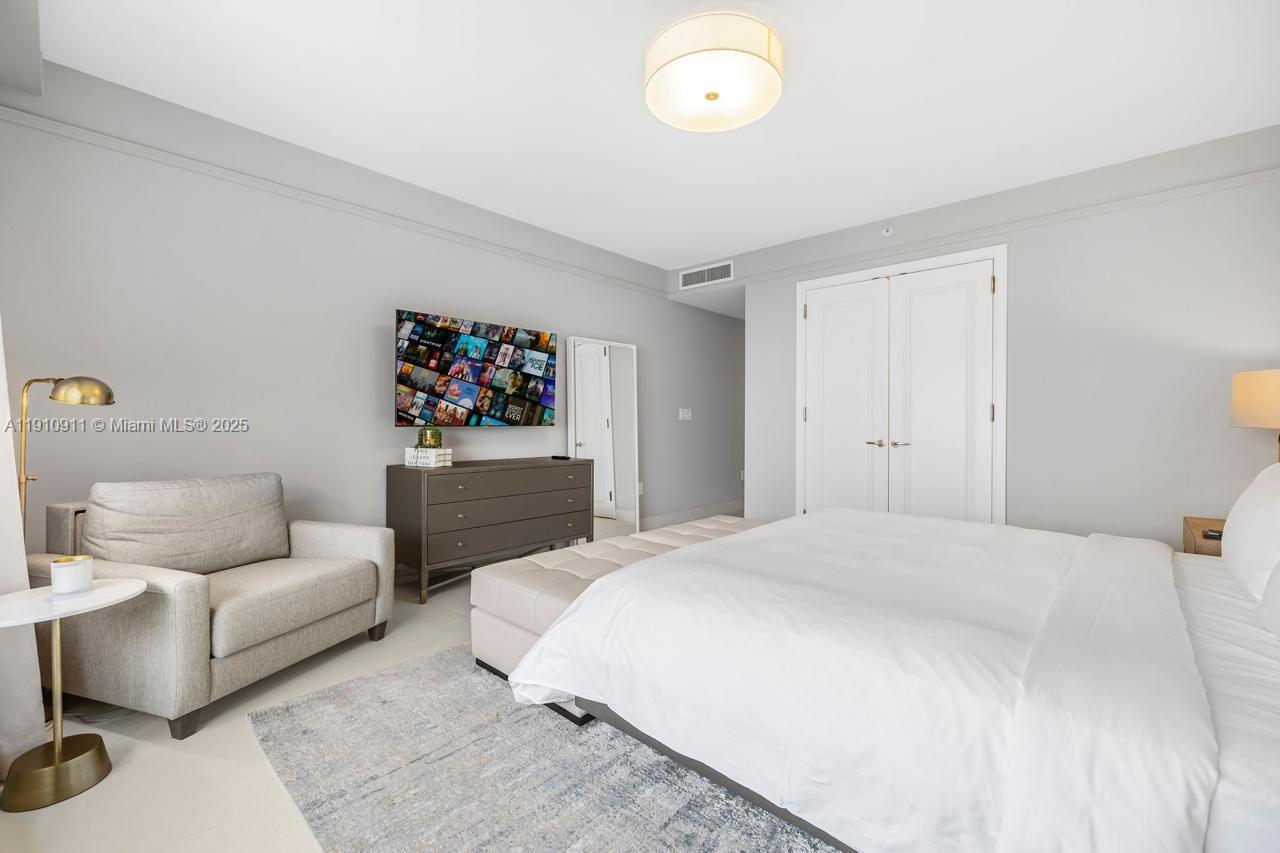 A bedroom features a bed with white bedding, a gray armchair, and a wall-mounted television — 1435 Brickell Ave # 3410, Miami FL 33131, MIAMI, FL