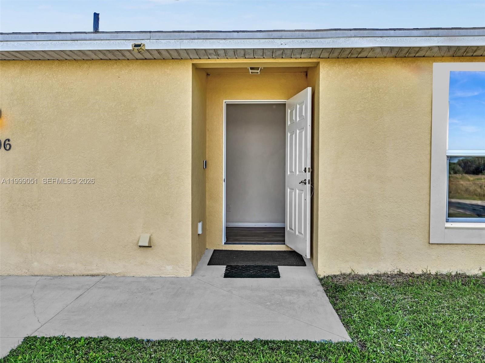 The exterior of a yellow stucco house features an open white front door — 9006 ABEL, La Belle FL 33935, LA BELLE, FL