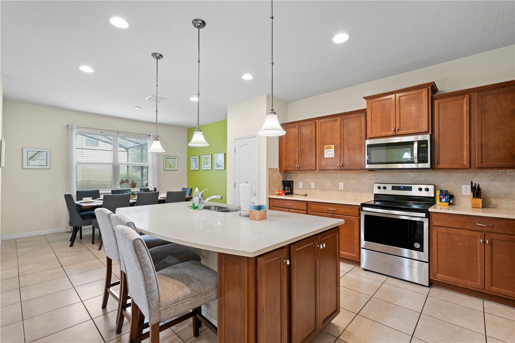 A kitchen features wood cabinets, stainless steel appliances, a large island, and an adjacent dining area — 1512 MUMBAI WAY, KISSIMMEE, FL
