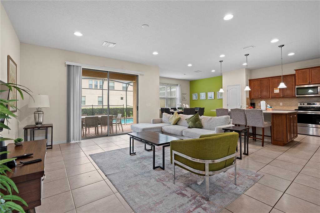 An open-concept living room and kitchen features tile flooring, a sectional sofa, and sliding doors — 1512 MUMBAI WAY, KISSIMMEE, FL