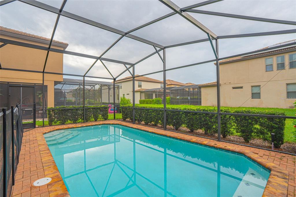 A swimming pool with a brick deck is enclosed by a screened lanai in a backyard — 1512 MUMBAI WAY, KISSIMMEE, FL