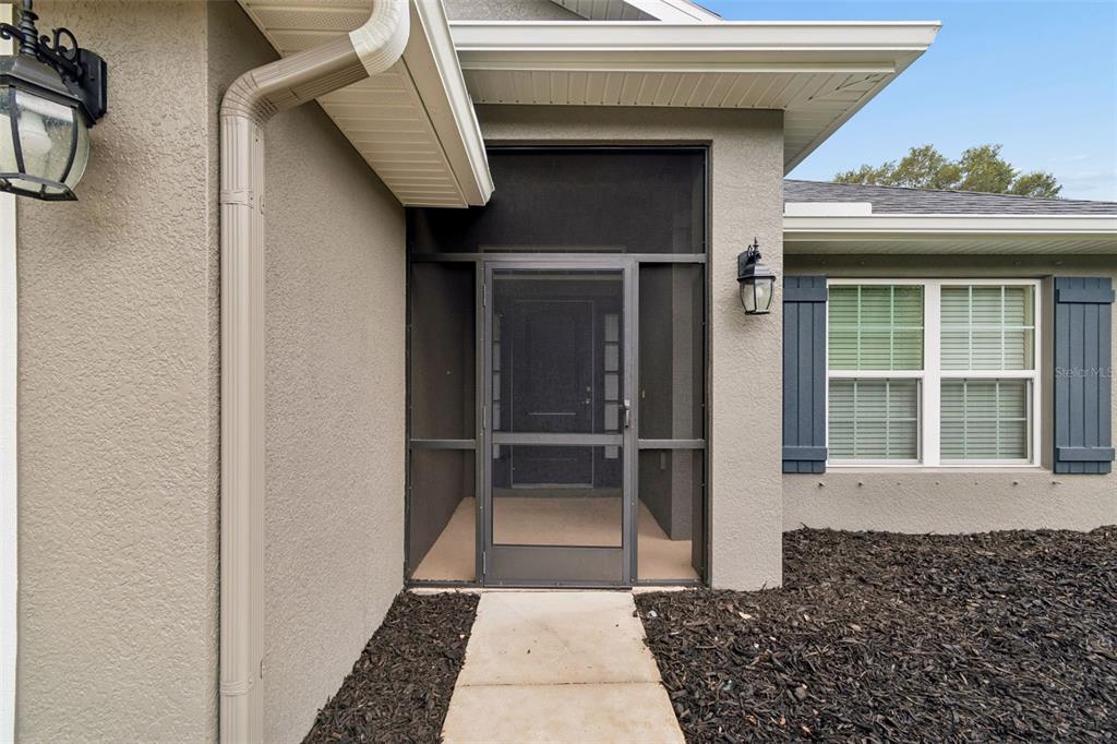 A beige house exterior features a screened front entryway, a concrete walkway, and dark shutters — 13428 MEADOW GOLF AVENUE, HUDSON, FL
