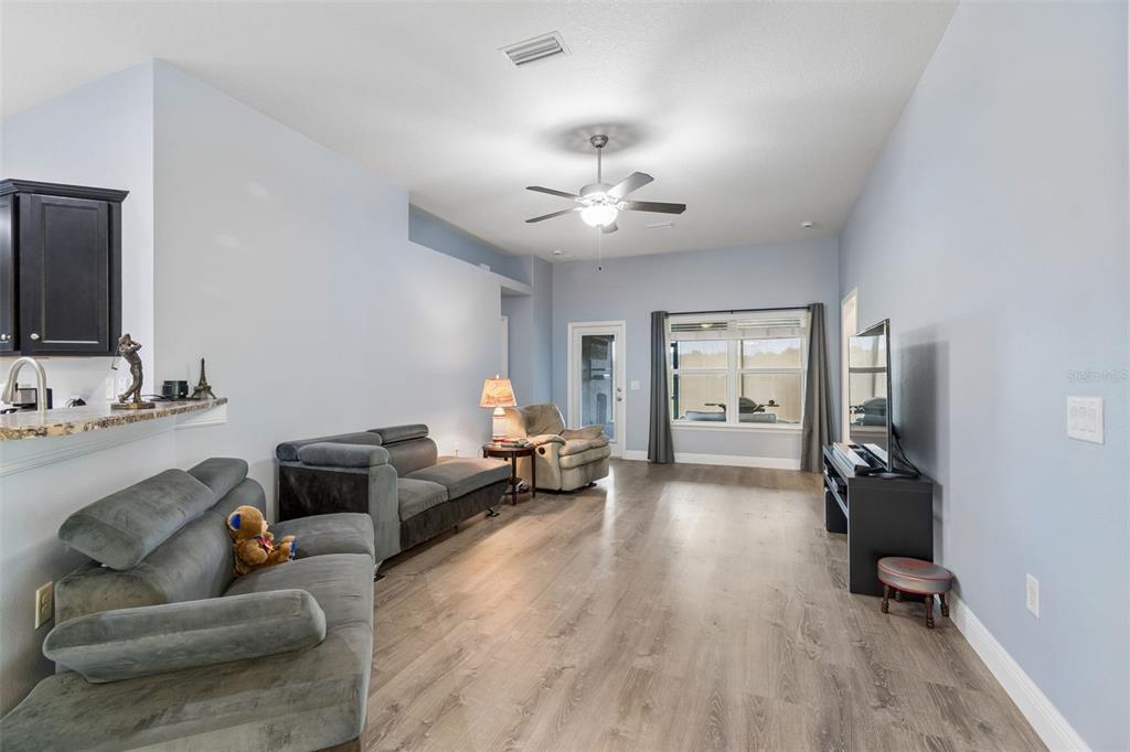 A living room features light blue walls, wood-look flooring, a ceiling fan, and gray sofas — 13428 MEADOW GOLF AVENUE, HUDSON, FL