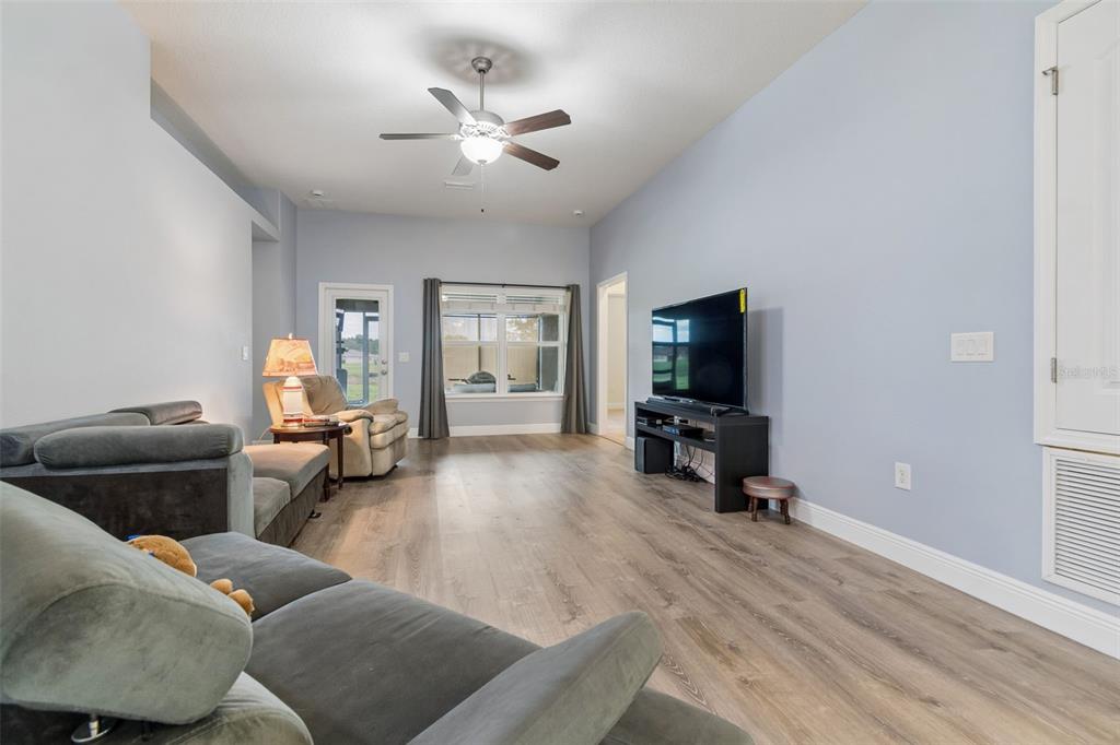 A living room features light blue walls, wood-look flooring, a ceiling fan, and a television — 13428 MEADOW GOLF AVENUE, HUDSON, FL