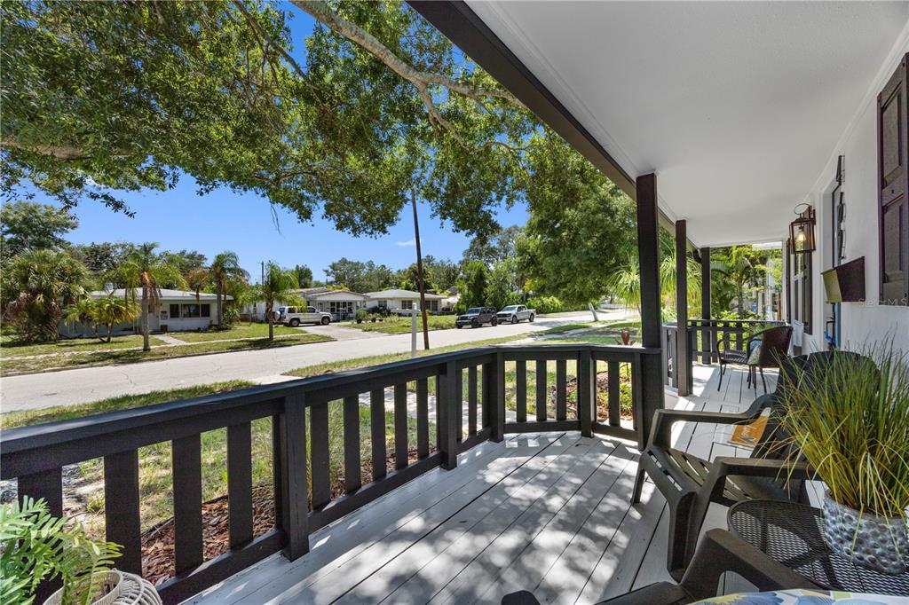 A covered wooden porch with dark railings overlooks a residential street with trees and houses — 4621 4TH AVENUE N, ST PETERSBURG, FL