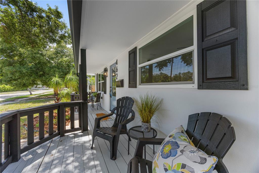 A covered porch with gray wooden decking, black railings, and two dark Adirondack chairs — 4621 4TH AVENUE N, ST PETERSBURG, FL