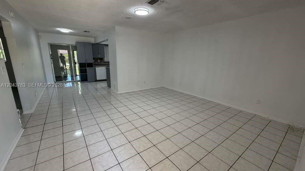 A room with white tiled floors and white walls leads to a kitchen area — 5425 NW 16th Ct # 0, Lauderhill FL 33313, LAUDERHILL, FL