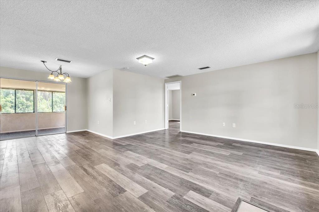 An empty living area features gray wood-look flooring, light walls, and a sliding glass door — 528 MAGNOLIA AVENUE NW, PORT CHARLOTTE, FL