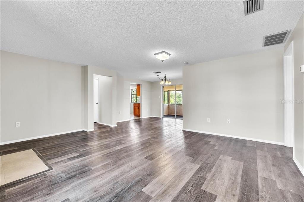 An open-concept living area features wood-look flooring, light walls, and a view into the kitchen — 528 MAGNOLIA AVENUE NW, PORT CHARLOTTE, FL