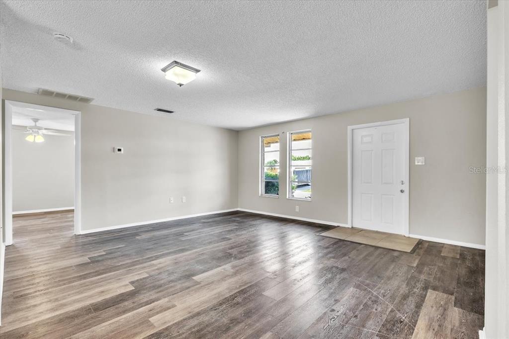 An empty living room features gray wood-look flooring, light-colored walls, two windows, and a door — 528 MAGNOLIA AVENUE NW, PORT CHARLOTTE, FL