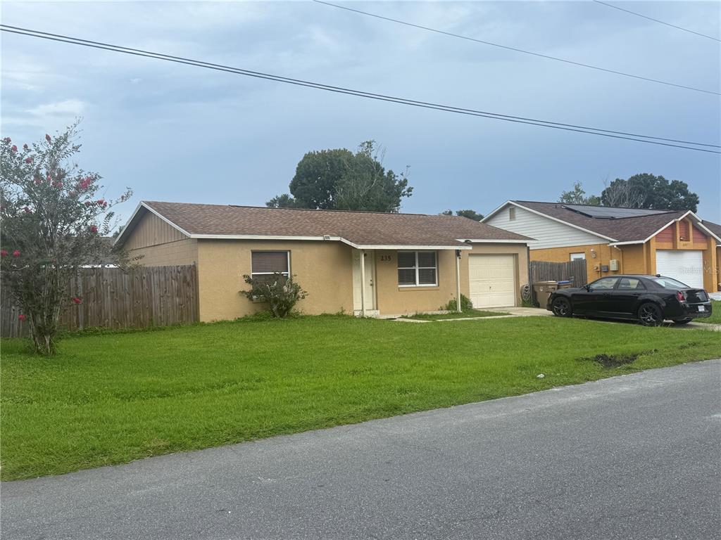A single-story tan house with a brown roof, a one-car garage, and a front lawn — 235 BALBOA DRIVE, KISSIMMEE, FL