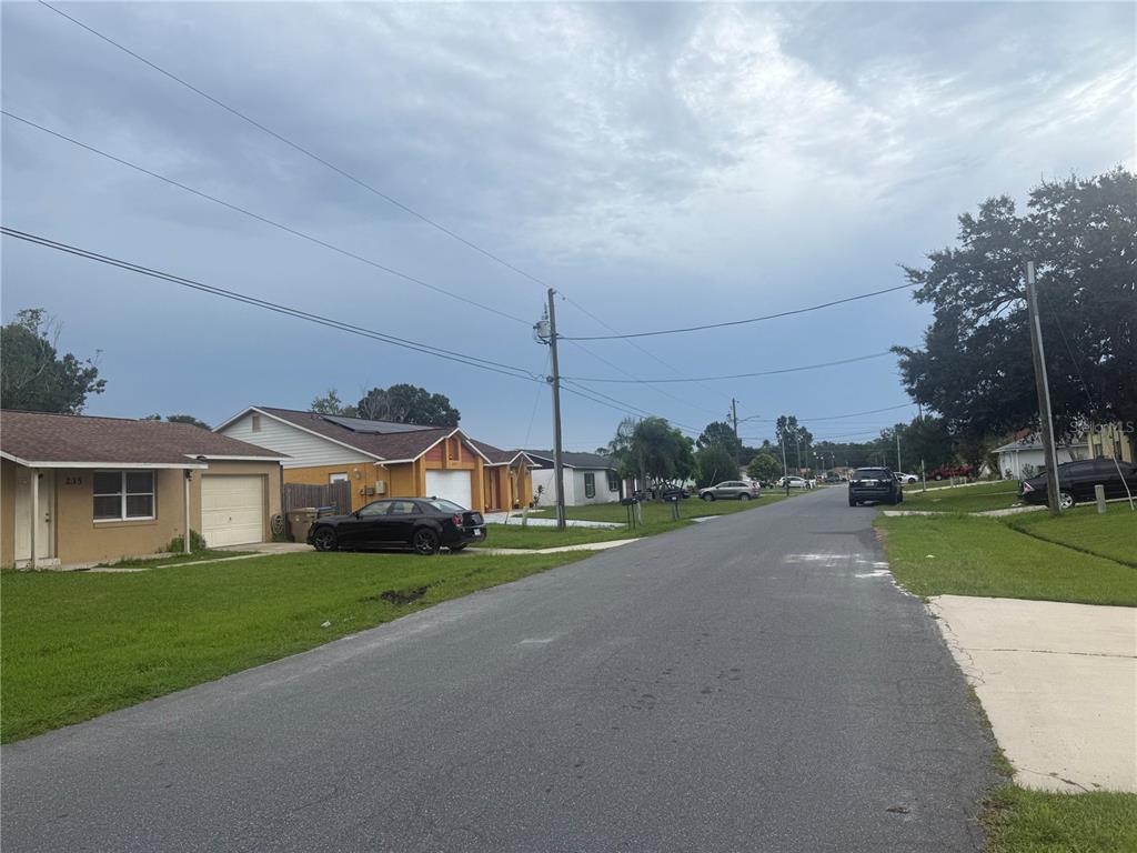 A residential street features single-story houses, parked cars, and utility poles under a cloudy sky — 235 BALBOA DRIVE, KISSIMMEE, FL