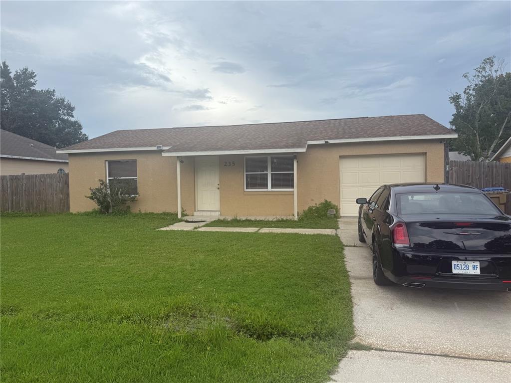 A single-story tan house with a brown roof, a garage, and a front lawn — 235 BALBOA DRIVE, KISSIMMEE, FL