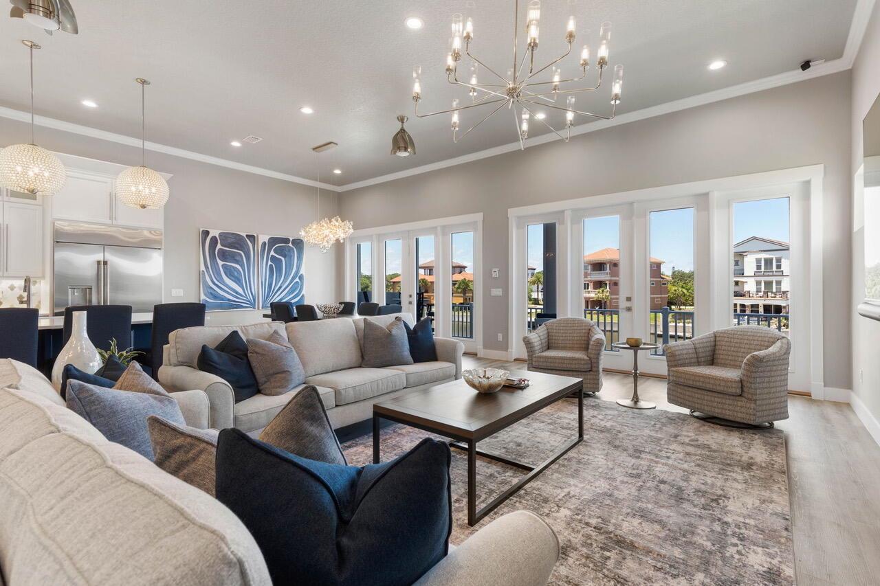 A bright living room features a large sectional, two armchairs, and glass doors overlooking buildings — 18 Spinaker Circle, Palm Coast FL 32137, PALM COAST, FL