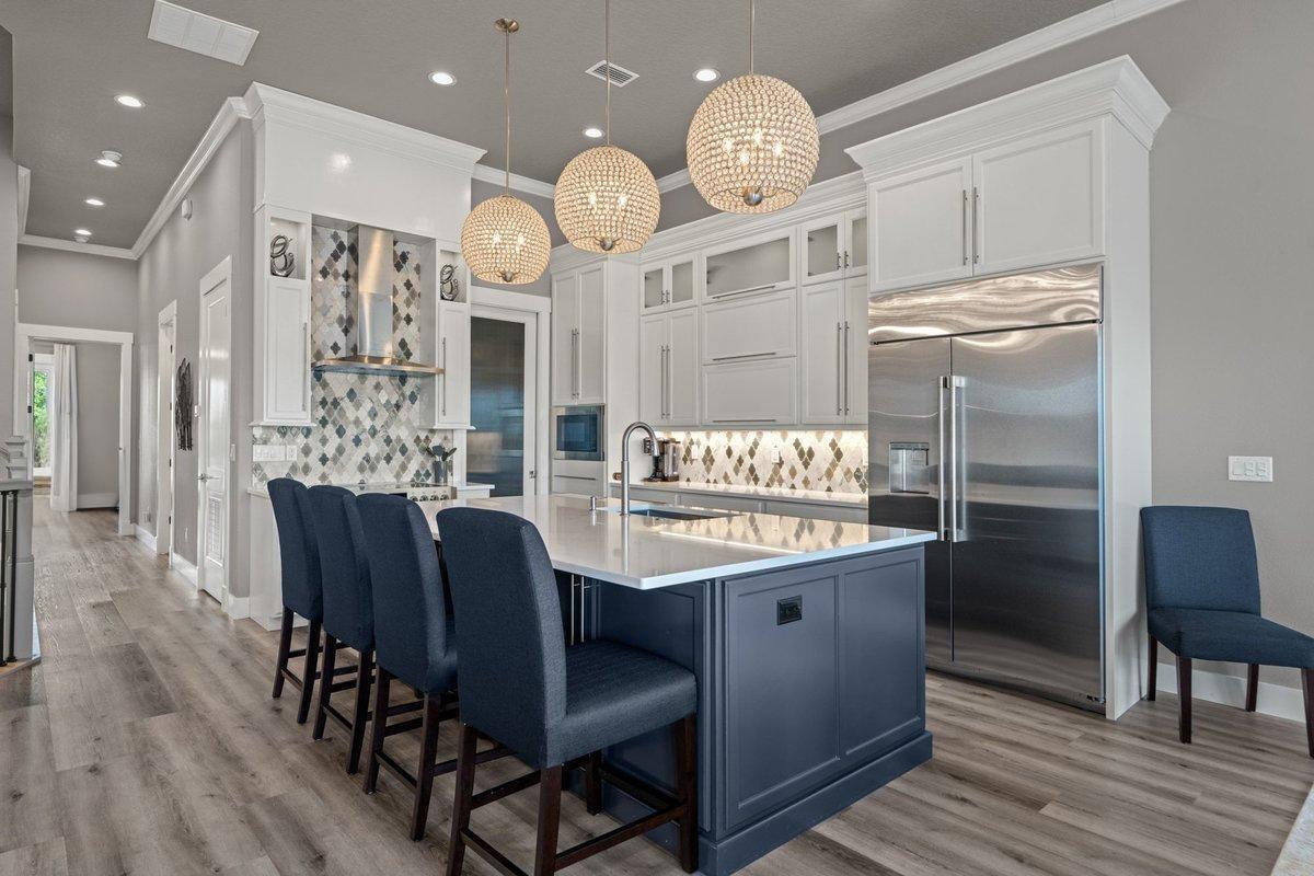 A kitchen features a dark blue island, white cabinetry, stainless steel appliances, and crystal pendants — 18 Spinaker Circle, Palm Coast FL 32137, PALM COAST, FL
