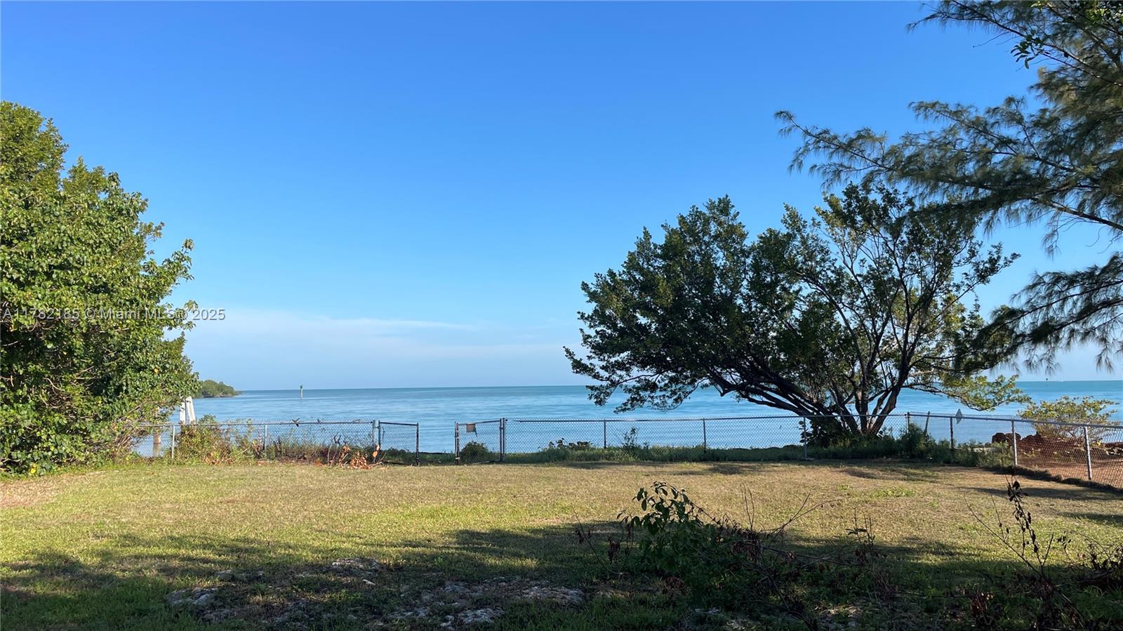 A grassy waterfront lot features a chain-link fence overlooking the ocean under a clear sky — 14 125th Street Gulf, Marathon FL 33050, MARATHON, FL