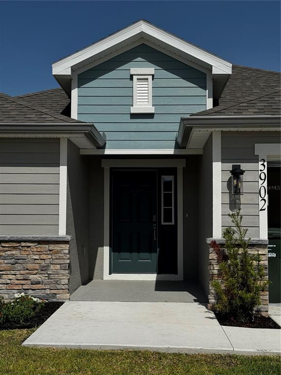 The exterior of a house features a teal gable, stone veneer, and a dark front door — 3902 WRENWOOD DRIVE, LAKELAND, FL