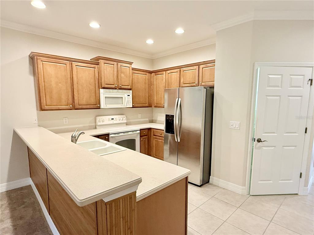A kitchen features wood cabinets, stainless steel appliances, and a white countertop breakfast bar — 11479 52ND COURT E, PARRISH, FL
