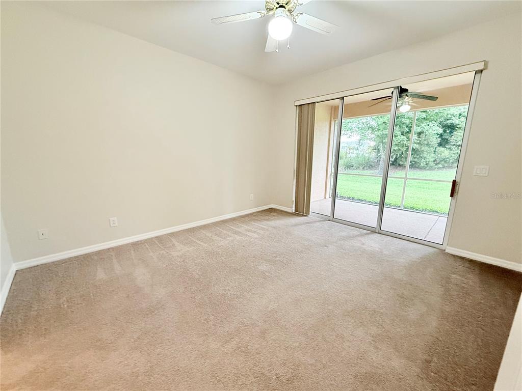 An empty bedroom features beige carpet, a ceiling fan, and sliding glass doors to a patio — 11479 52ND COURT E, PARRISH, FL