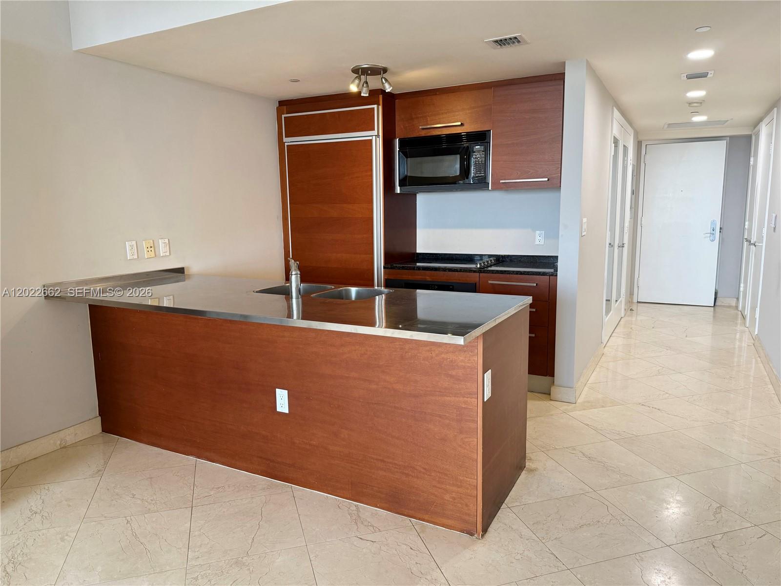 A kitchen features a stainless steel countertop island, wood cabinetry, and light-colored tile flooring — 1850 S OCEAN DR # 4009, Hallandale Beach FL 33009, HALLANDALE BEACH, FL