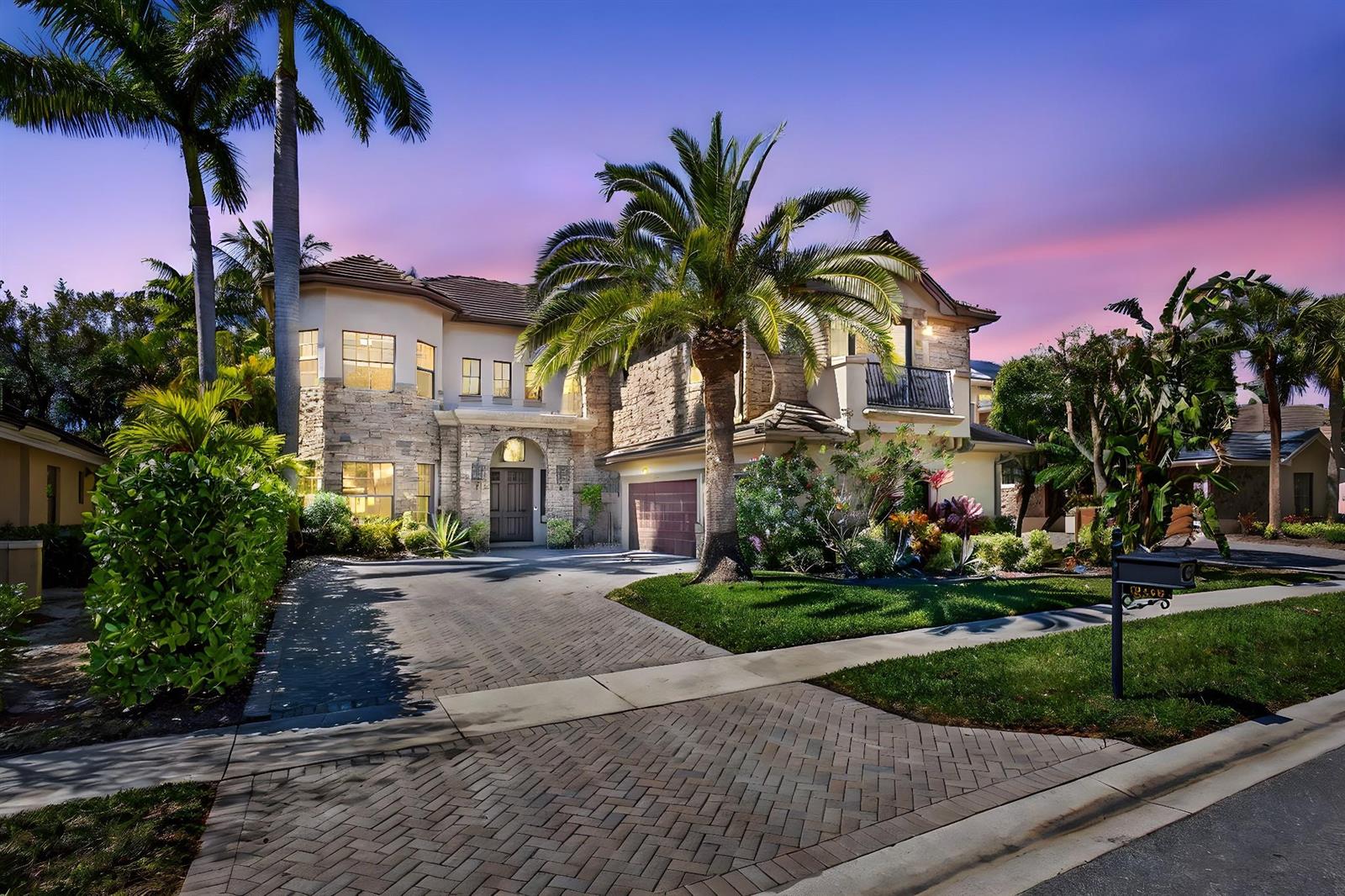 A two-story stone and stucco house features a paved driveway and palm trees at dusk — 10468 Trianon Place, Wellington FL 33449, WELLINGTON, FL