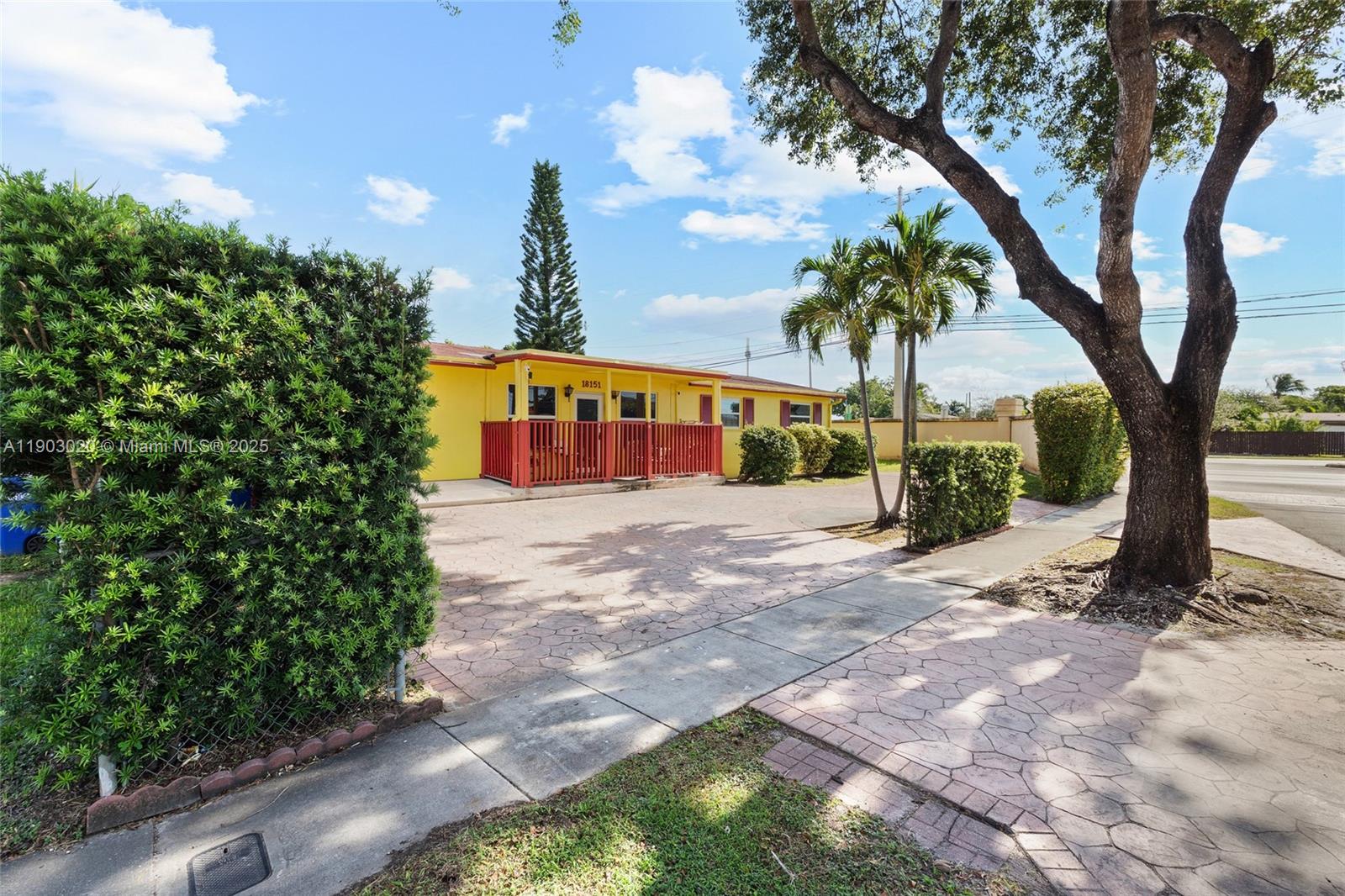 A yellow single-story house features a red-railed front porch and a paved driveway — 18151 NE 9th Ct, North Miami Beach FL 33162, NORTH MIAMI BEACH, FL