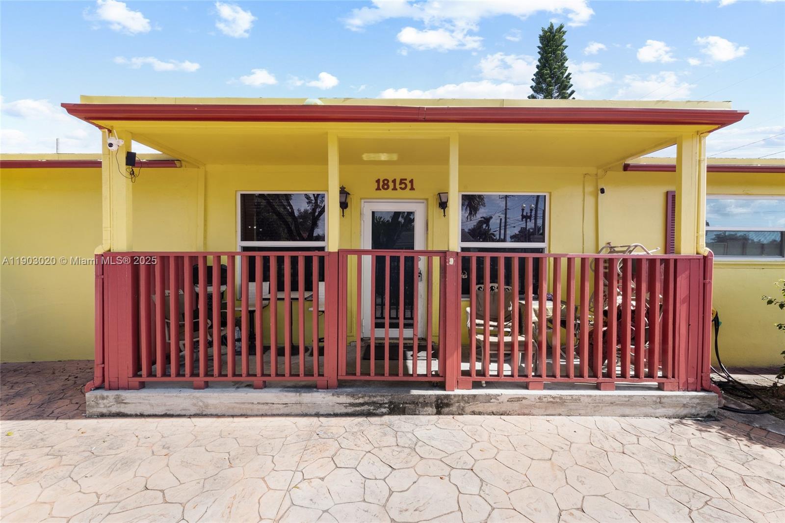 A yellow house exterior features a covered porch with red railings and a front door — 18151 NE 9th Ct, North Miami Beach FL 33162, NORTH MIAMI BEACH, FL