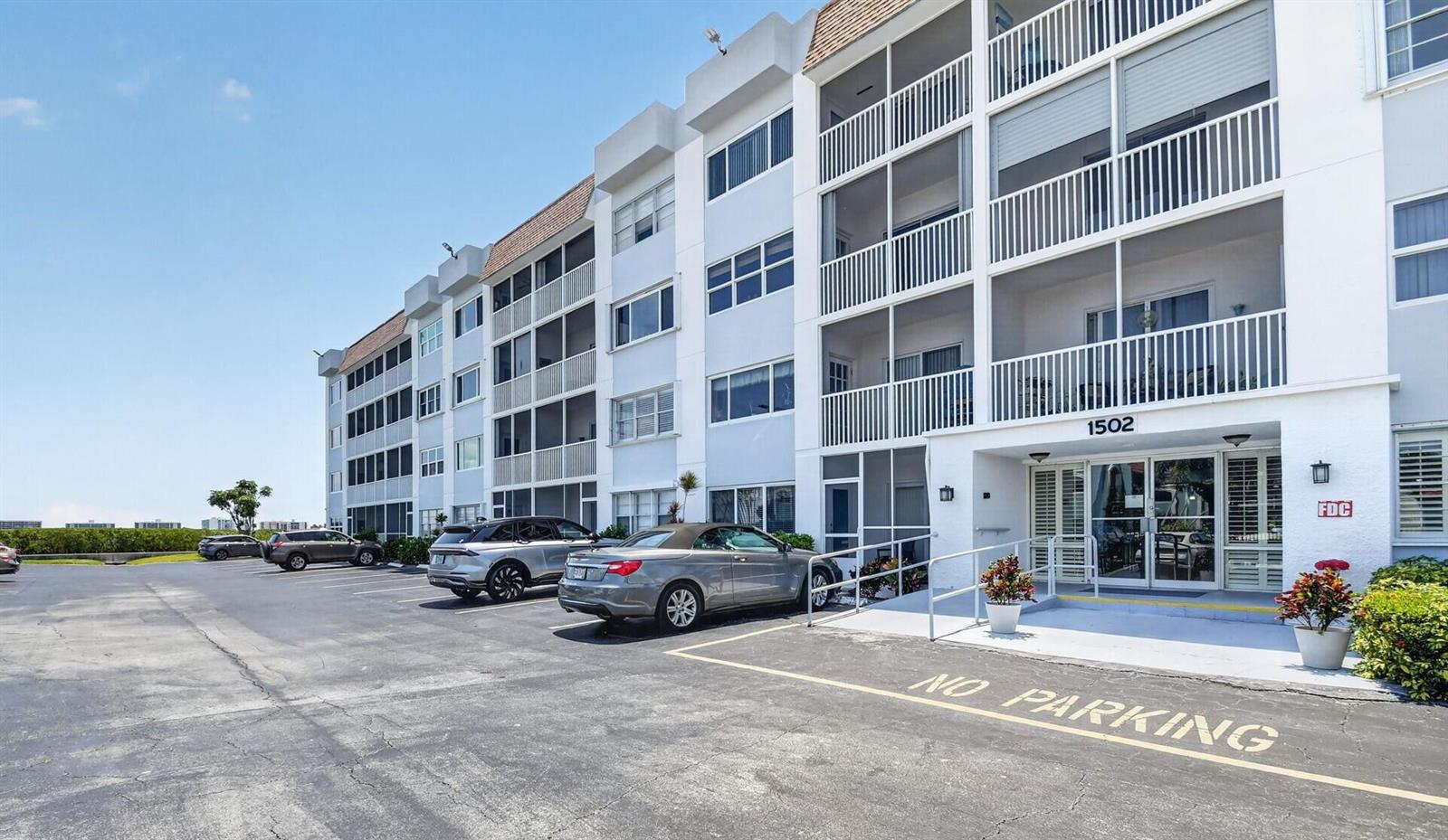 The exterior of a multi-story apartment building features a parking lot and a main entrance — 1502 S Lakeside Drive # 214, FL 33460, FL
