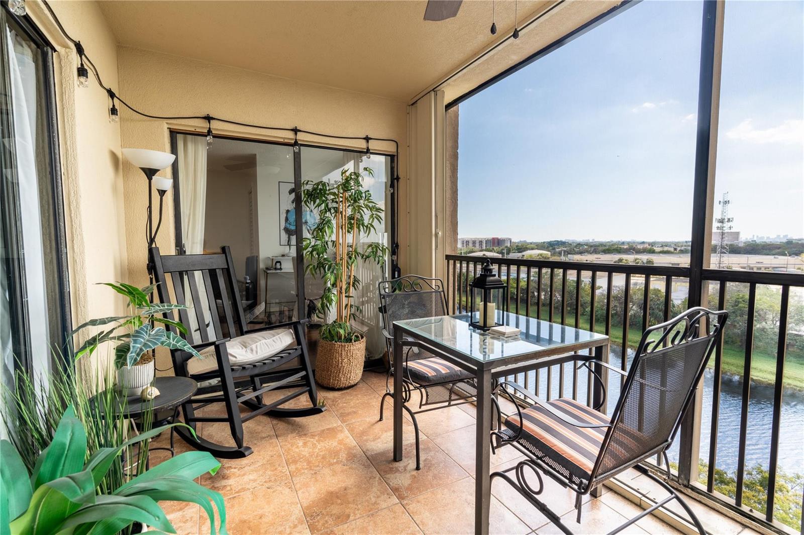 A screened-in balcony features tile flooring, a dining set, a rocking chair, and water views — 2206 S Cypress Bend Drive # 803, Pompano Beach FL 33069, POMPANO BEACH, FL