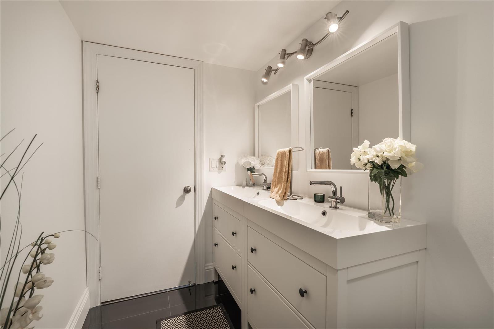 A white double vanity with two sinks and mirrors sits in a bathroom with dark floors — 2206 S Cypress Bend Drive # 803, Pompano Beach FL 33069, POMPANO BEACH, FL