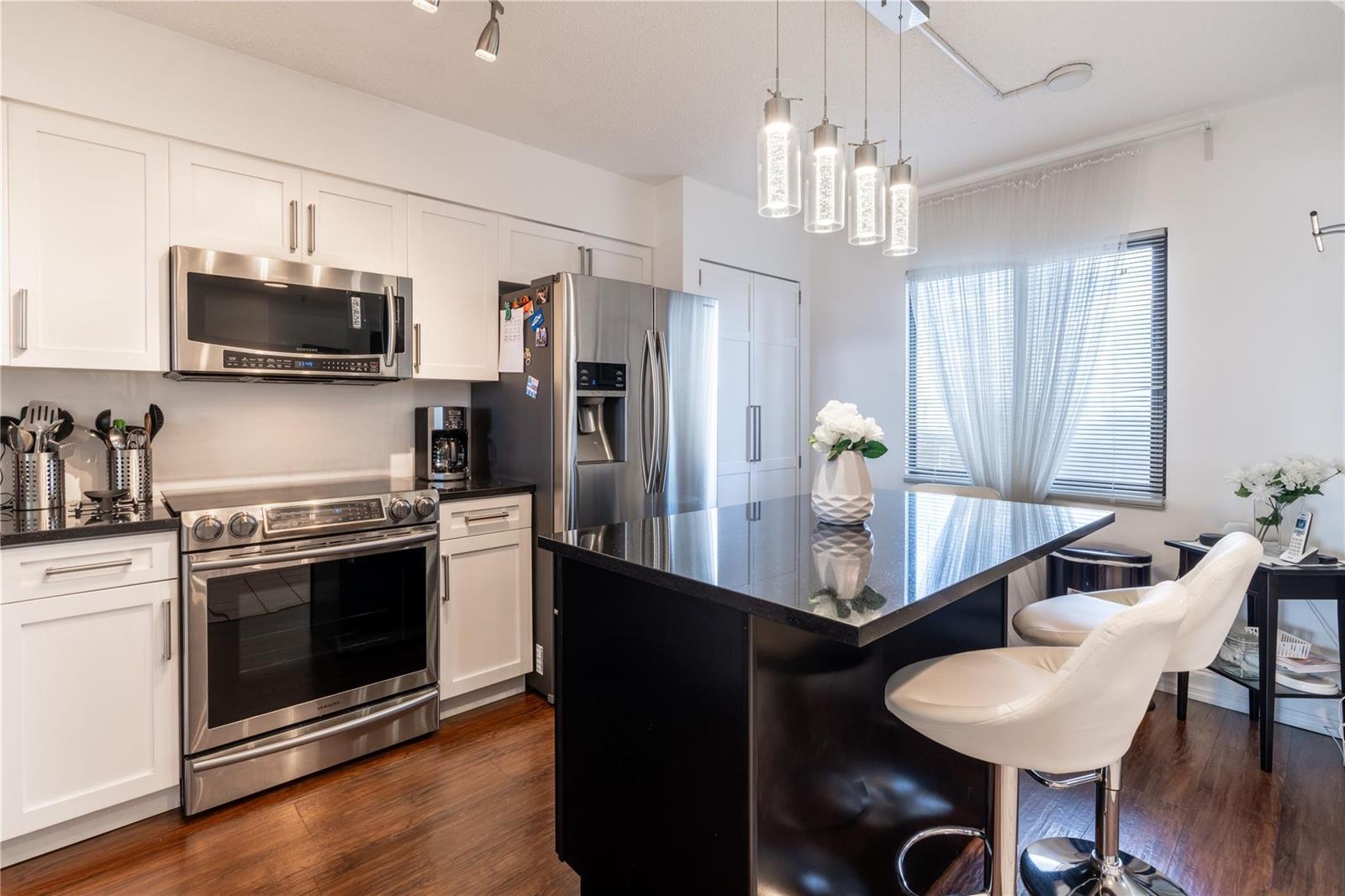 A kitchen with white cabinets, stainless steel appliances, a black island, and wood flooring — 2206 S Cypress Bend Drive # 803, Pompano Beach FL 33069, POMPANO BEACH, FL
