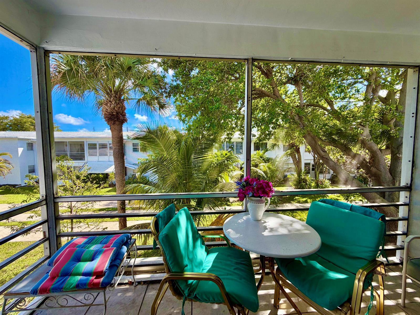 A screened-in porch features two teal chairs, a small round table, and tropical outdoor views — 2551 W Golf Boulevard # 204, Pompano Beach FL 33064, POMPANO BEACH, FL