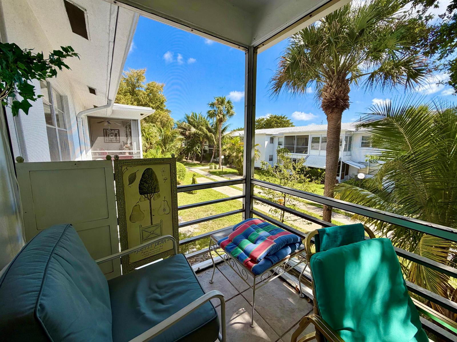 A screened-in balcony with outdoor furniture overlooks a grassy courtyard with palm trees — 2551 W Golf Boulevard # 204, Pompano Beach FL 33064, POMPANO BEACH, FL