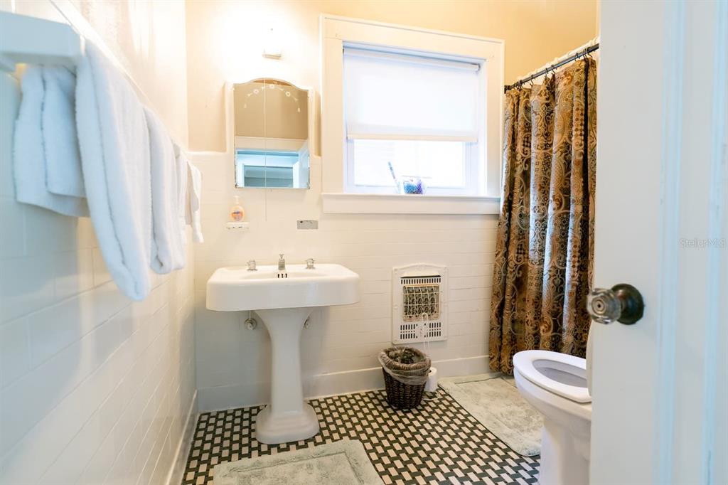 A bathroom features a pedestal sink, a patterned shower curtain, and black-and-white checkered floor tiles — 1200 W LAKE OTIS DRIVE SE, WINTER HAVEN, FL