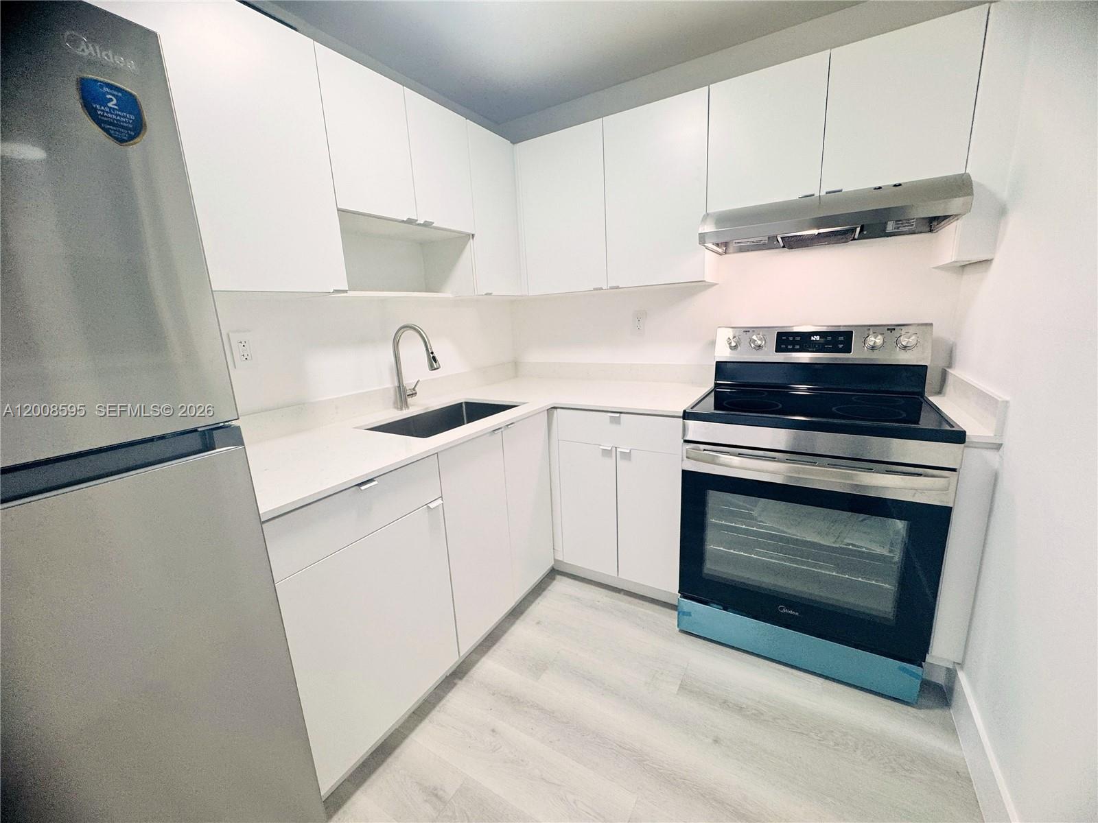 An empty room features white walls, light-colored wood-look flooring, and a sliding glass balcony door — 6095 W 18th Ave # S219, Hialeah FL 33012, HIALEAH, FL