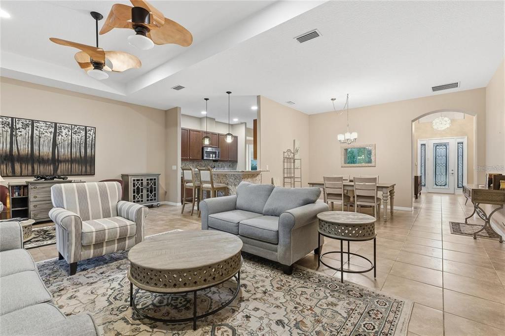 A spacious open-concept living room features a kitchen, dining area, and neutral tile flooring — 8683 BRIDGEPORT BAY CIRCLE, MOUNT DORA, FL