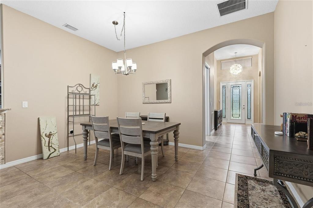 A dining room with tile floors, a wooden table, and an arched entryway to the foyer — 8683 BRIDGEPORT BAY CIRCLE, MOUNT DORA, FL