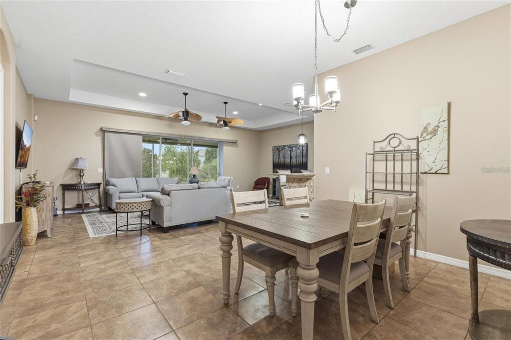 An open-concept living and dining area features tile flooring, a tray ceiling, and neutral walls — 8683 BRIDGEPORT BAY CIRCLE, MOUNT DORA, FL