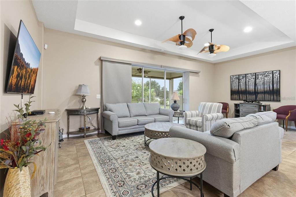 A living room features a tray ceiling, two ceiling fans, tile floors, and sliding glass doors — 8683 BRIDGEPORT BAY CIRCLE, MOUNT DORA, FL