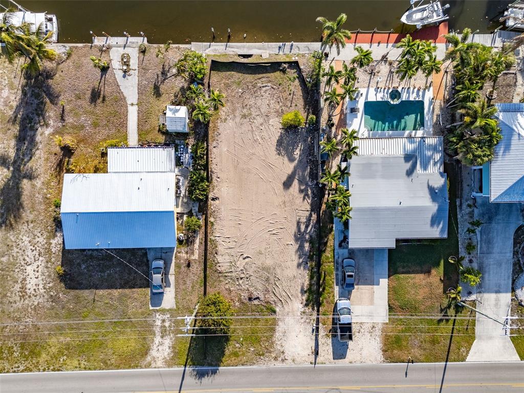 An aerial view shows a vacant residential lot situated between two houses along a canal — 3314 YORK ROAD, ST JAMES CITY, FL