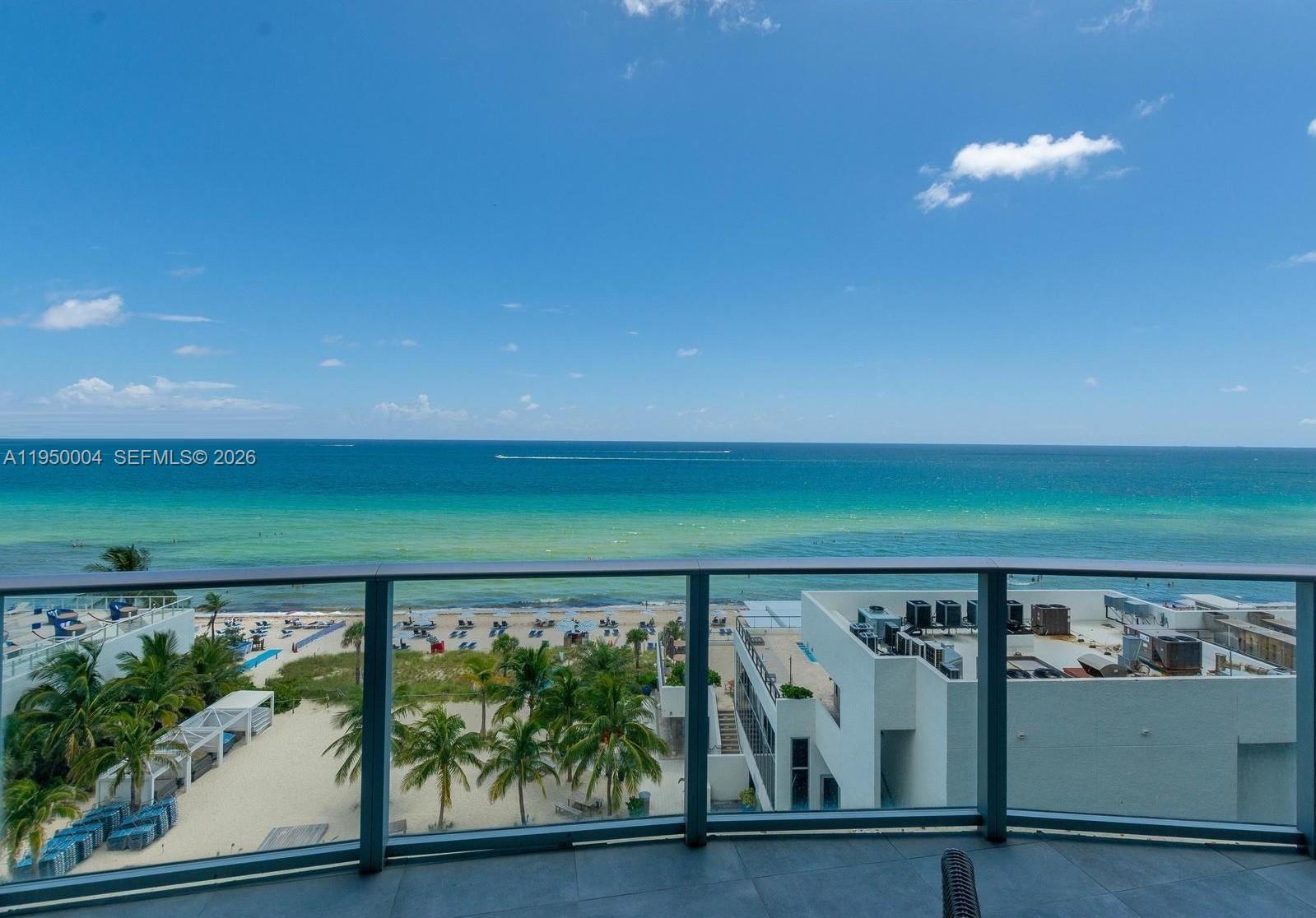 A balcony overlooks a sandy beach, palm trees, and the ocean under a blue sky — 4111 S Ocean Dr # 601, Hollywood FL 33019, HOLLYWOOD, FL