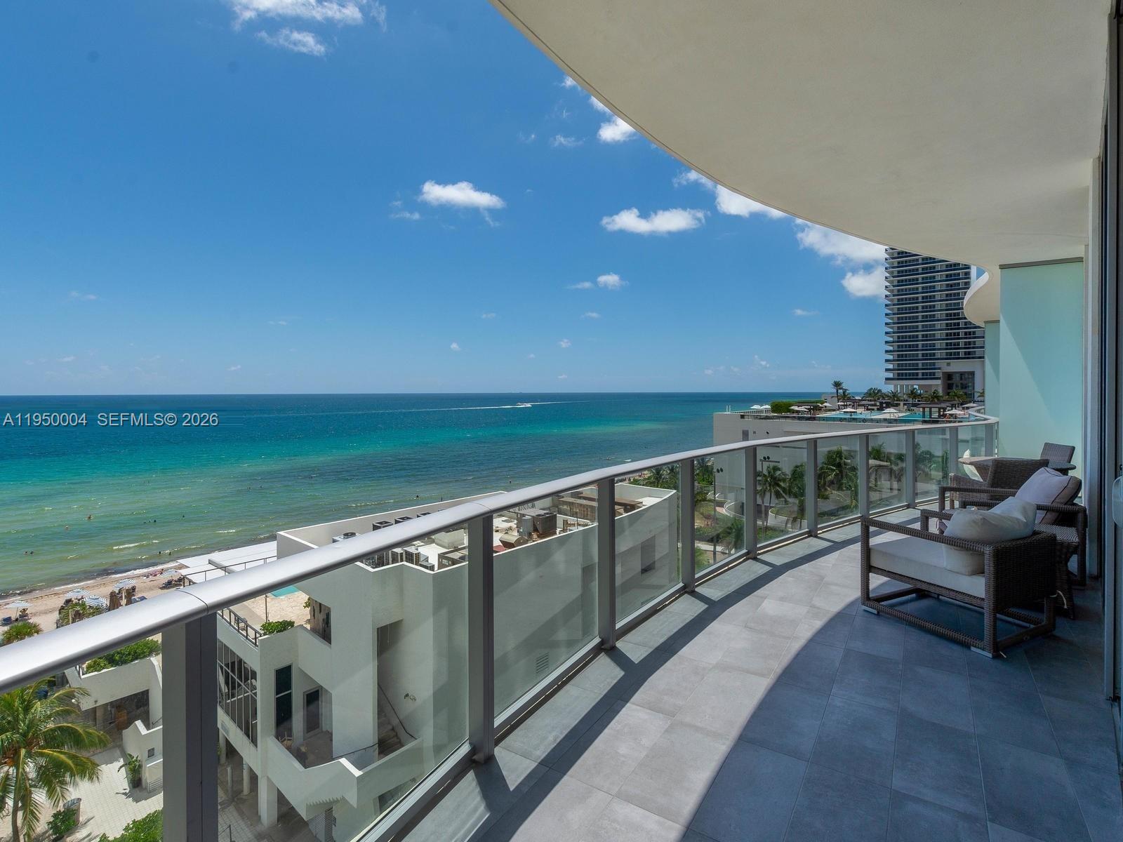 A balcony with glass railings overlooks the ocean and a nearby building — 4111 S Ocean Dr # 601, Hollywood FL 33019, HOLLYWOOD, FL
