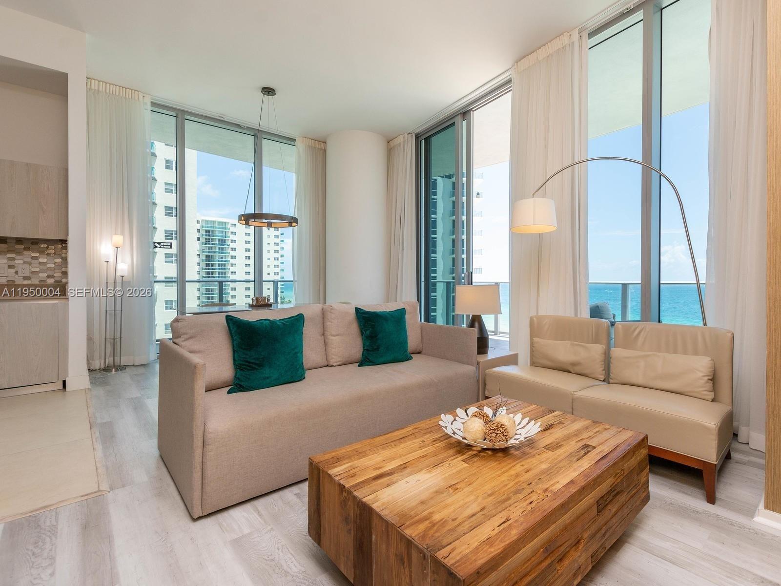 A living room features a beige sofa, leather loveseat, wooden coffee table, and floor-to-ceiling windows — 4111 S Ocean Dr # 601, Hollywood FL 33019, HOLLYWOOD, FL