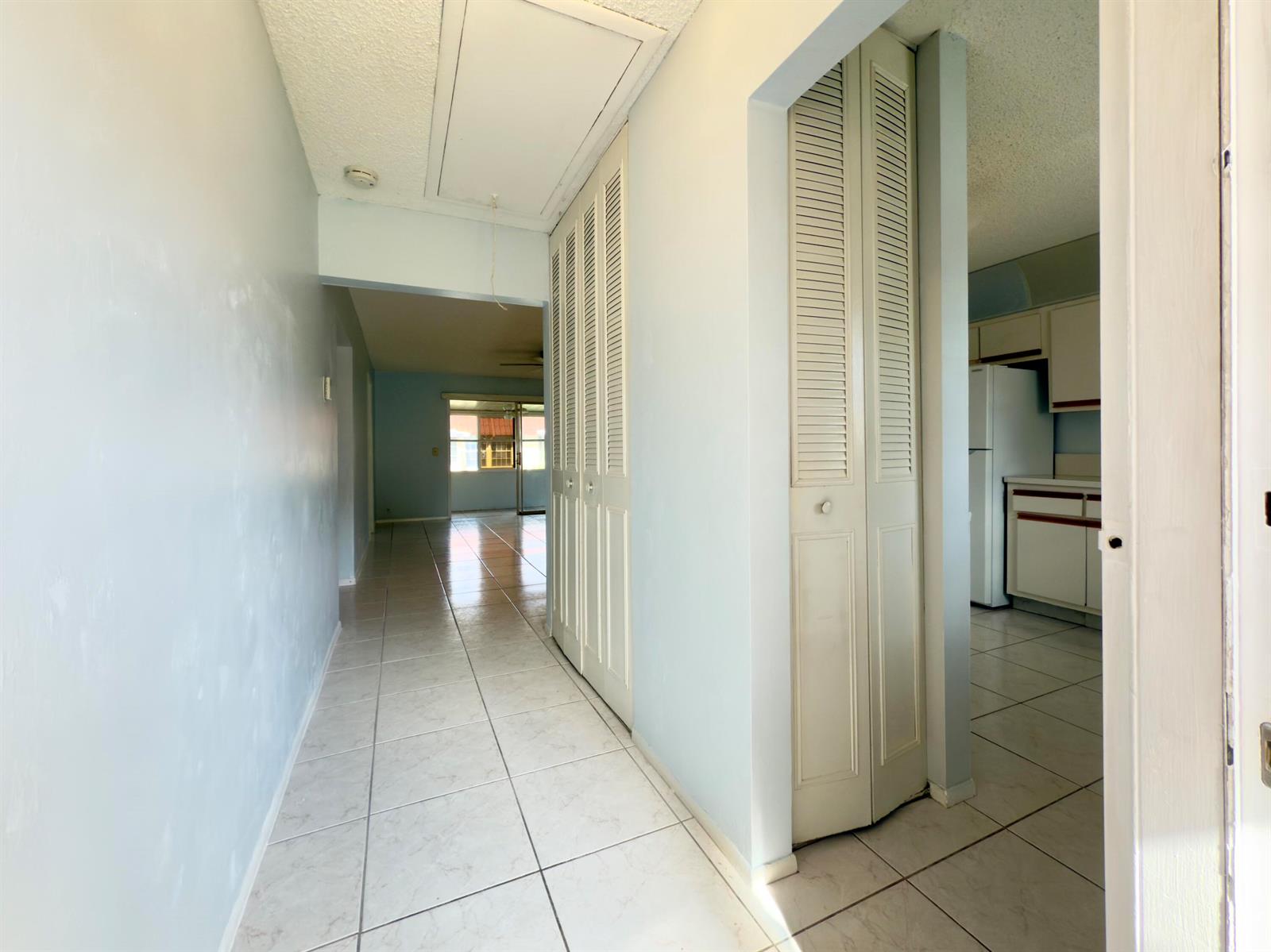 A hallway with white tile floors leads to a living area past louvered closet doors — 170 Amherst Lane, Lake Worth FL 33467, LAKE WORTH, FL
