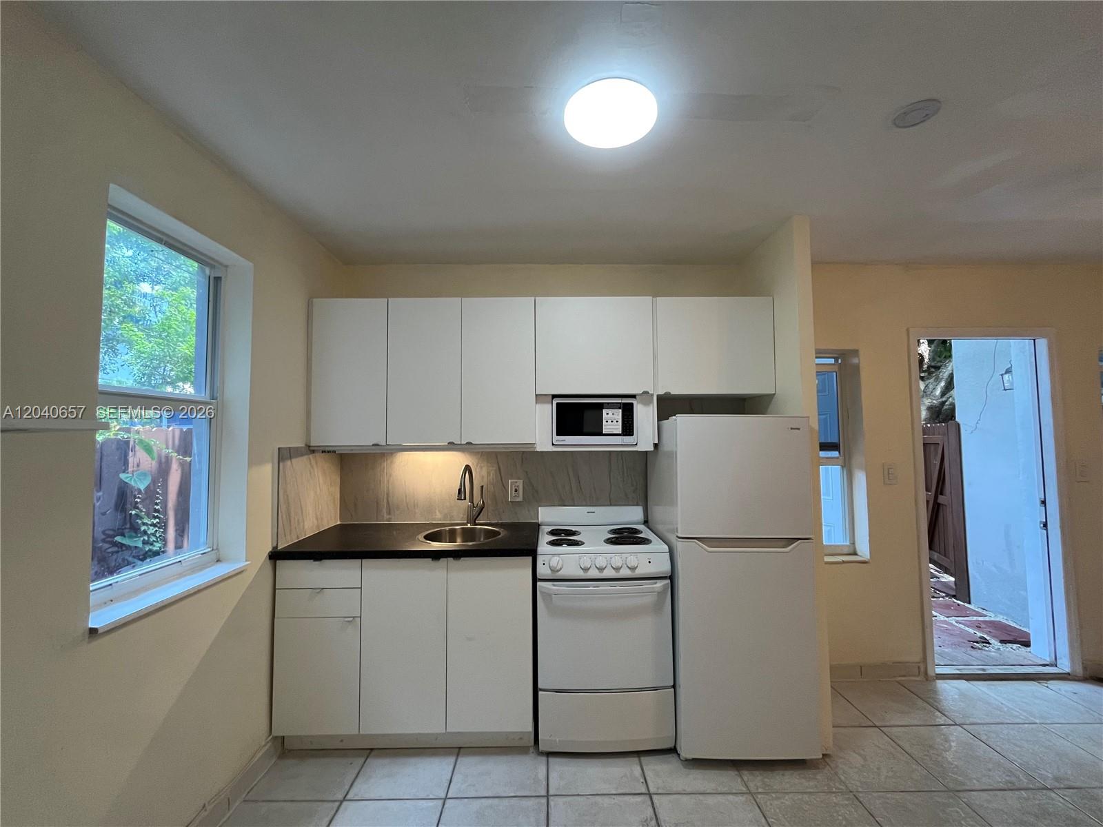 A small kitchen features white cabinets, a black countertop, a stove, and a refrigerator — 820 SW 31st Ave, Miami FL 33135, MIAMI, FL