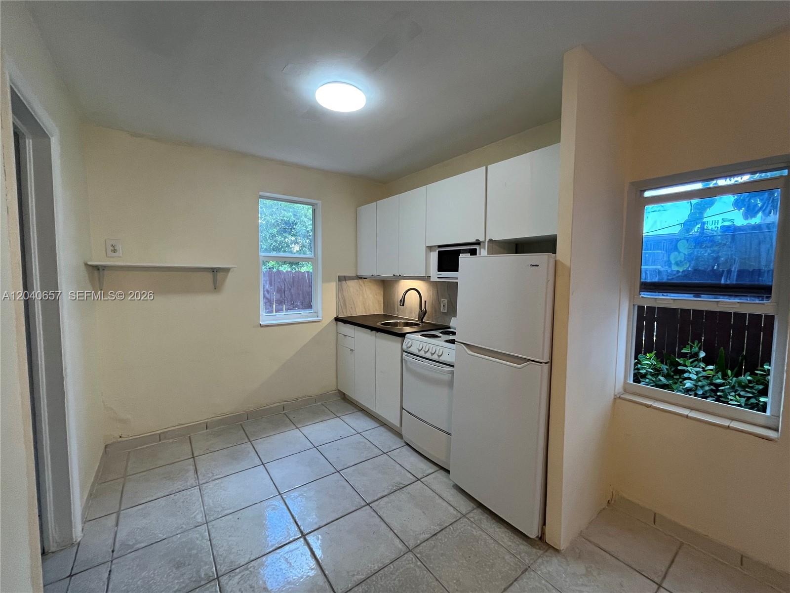 A small kitchen features white cabinets, a white stove, a refrigerator, and tiled flooring — 820 SW 31st Ave, Miami FL 33135, MIAMI, FL