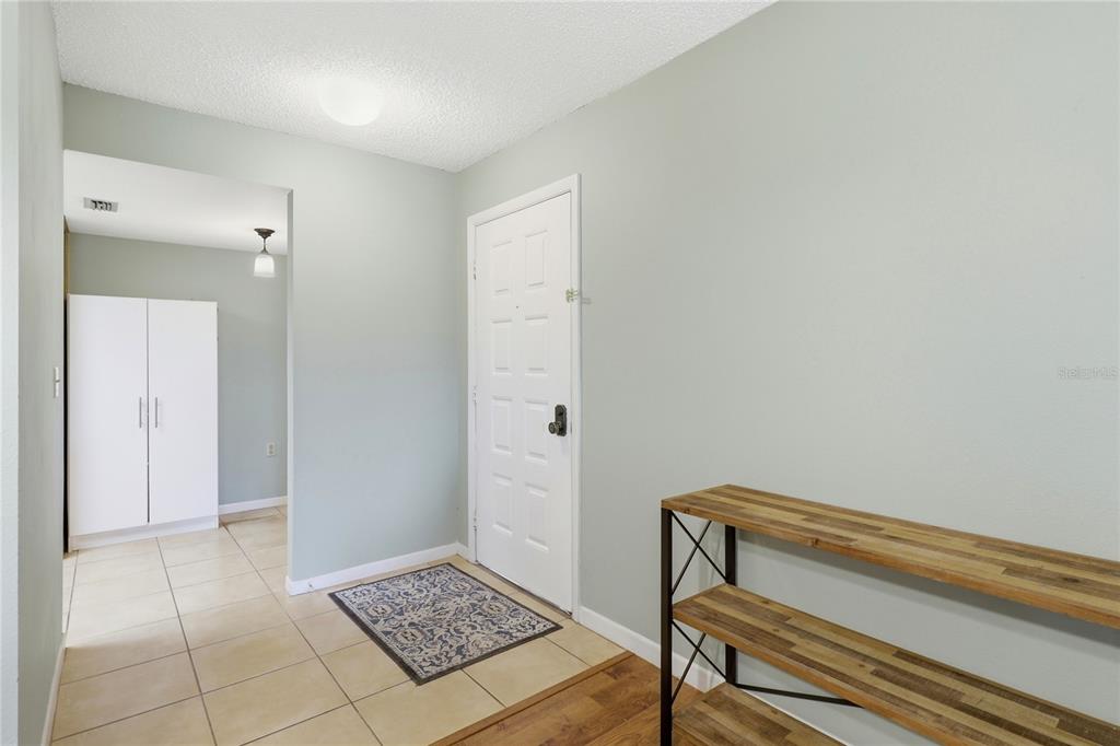 An entryway features light green walls, tiled flooring, a white door, and a wooden shelf — 2685 SABAL SPRINGS CIRCLE UNIT 105, CLEARWATER, FL