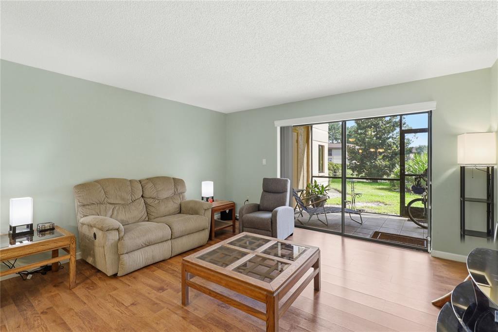 A living room with light green walls, wood flooring, a sofa, and a sliding glass door — 2685 SABAL SPRINGS CIRCLE UNIT 105, CLEARWATER, FL